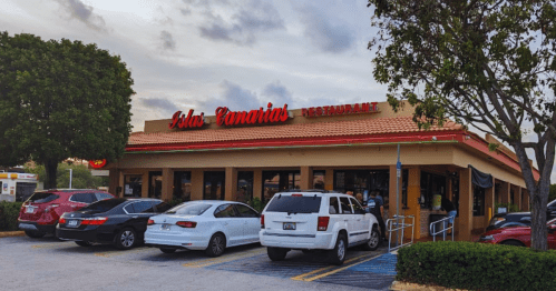 Exterior of Isla Canarias Restaurant with parked cars and trees, under a cloudy sky.
