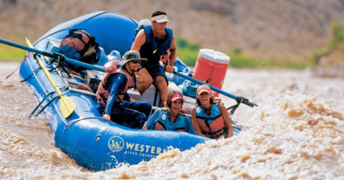 A group of five people navigating a blue raft through turbulent waters, enjoying a river adventure.