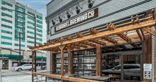 Exterior of 10 Barrel Brewing Co. featuring a wooden patio and urban buildings in the background.
