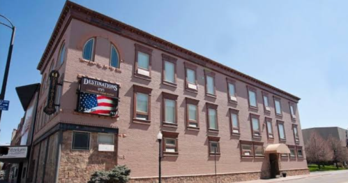 A brick building with large windows and an American flag sign, under a clear blue sky.