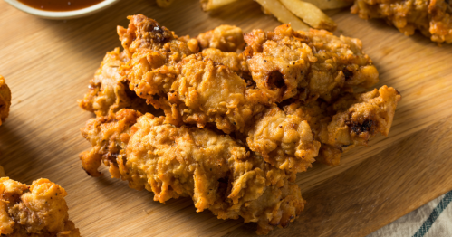 Crispy fried chicken pieces on a wooden platter, served with dipping sauce and fries.