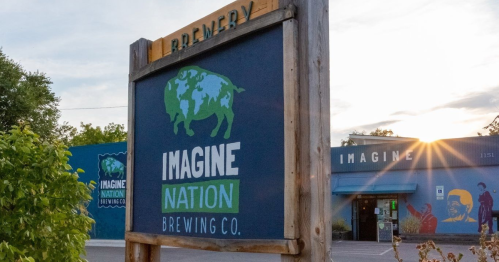 Sign for Imagine Nation Brewing Co. with a colorful mural and a setting sun in the background.