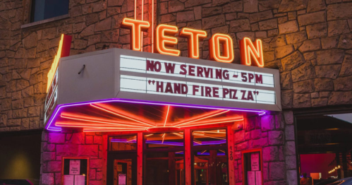 Neon-lit entrance of Teton restaurant with a marquee announcing "Now Serving - 5 PM Hand Fire Piz Za."