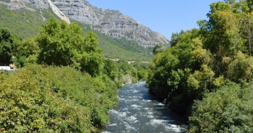 A flowing river surrounded by lush greenery and mountains under a clear blue sky.