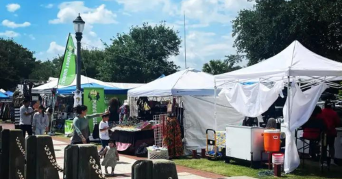 A vibrant outdoor market with tents, vendors, and visitors enjoying the sunny day.