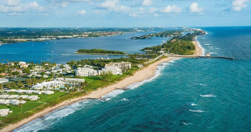 Aerial view of a coastal landscape with sandy beaches, lush greenery, and calm blue waters under a partly cloudy sky.
