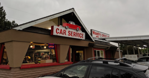 A car service building with a red sign, "CAR SERVICE," and "Woody's Drive-In" above, under a cloudy sky.