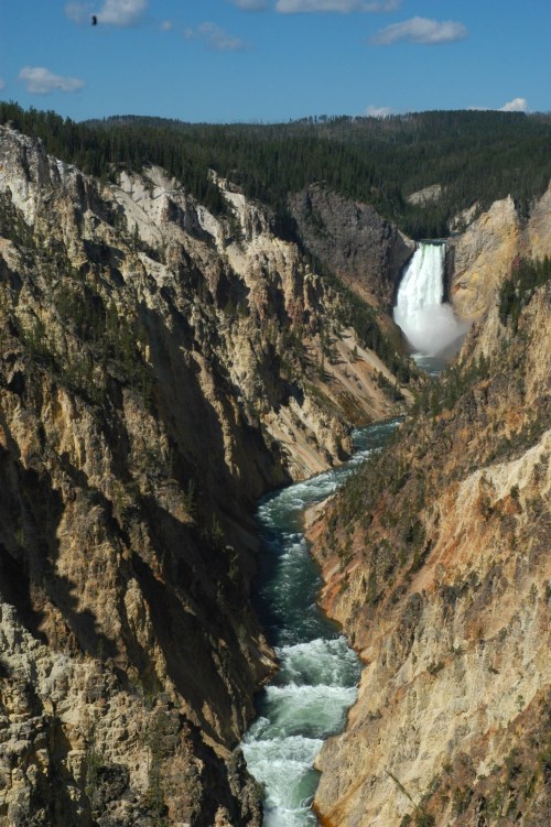 A stunning view of a waterfall cascading into a river, surrounded by steep, rocky cliffs and lush greenery.