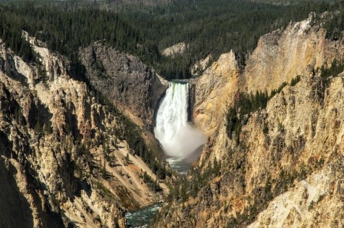 A stunning waterfall cascades down rocky cliffs, surrounded by lush green trees in a scenic landscape.