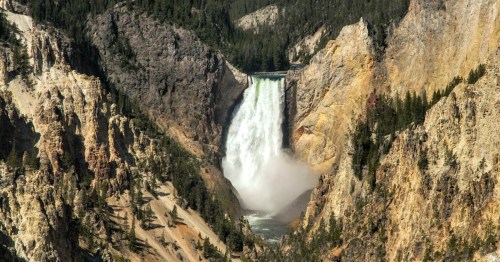 A stunning waterfall cascades down rocky cliffs, surrounded by lush greenery and rugged terrain.