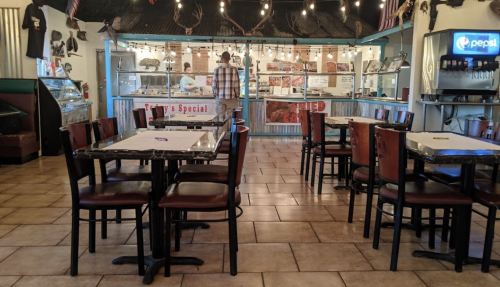 Interior of a casual dining restaurant with empty tables and a counter displaying food options in the background.