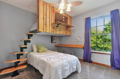 Cozy bedroom with a lofted bed, wooden stairs, and a large window with purple curtains.