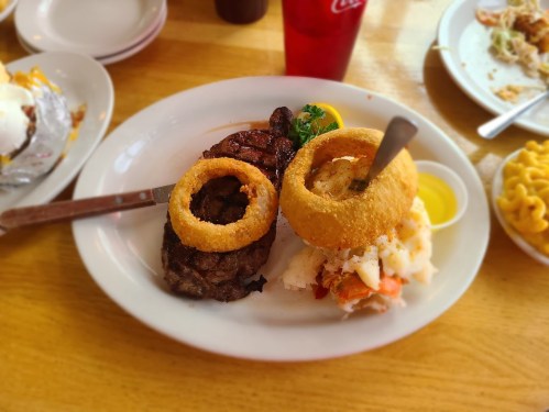 A plate featuring a steak with two onion rings, mashed potatoes, and a side of dipping sauce.