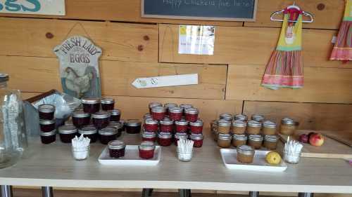 A wooden table displays jars of jam and fresh eggs, with utensils and fruit, against a rustic wooden backdrop.