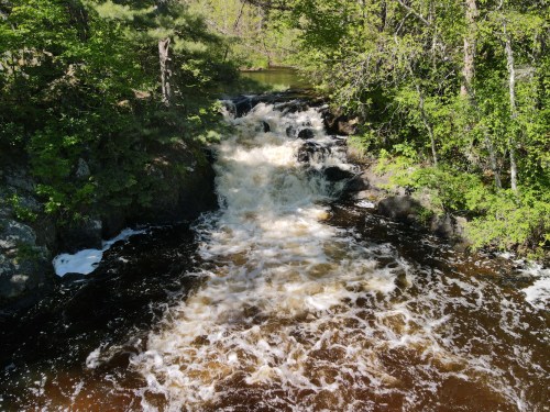 A flowing river cascades over rocks, surrounded by lush green trees and a serene natural landscape.