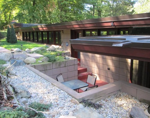 A modern building with large windows, surrounded by greenery and a stone pathway leading to a small outdoor seating area.
