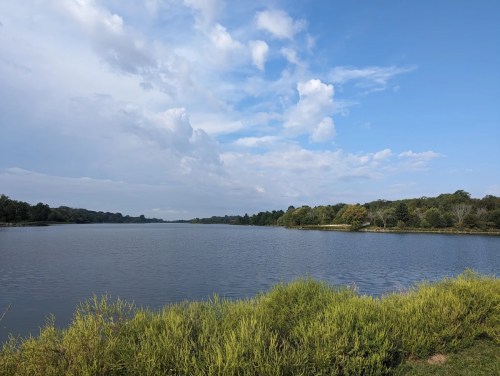 A serene river scene with lush greenery along the banks under a partly cloudy sky.