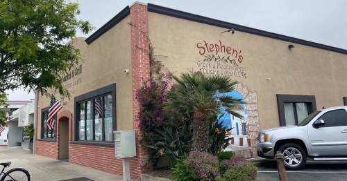 Exterior of Stephen's Greek & Mediterranean restaurant, featuring a mural and American flags, surrounded by greenery.