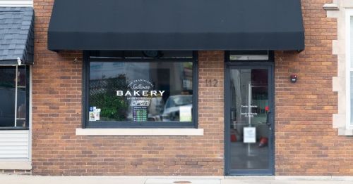A bakery storefront with a black awning and large window displaying the word "Bakery" on a brick building.