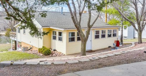 A yellow house with multiple windows, surrounded by trees and a landscaped path, set in a peaceful outdoor environment.
