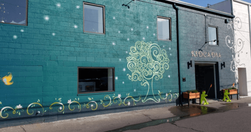 Colorful mural on a building featuring a tree design and decorative swirls, with a bright blue and green background.