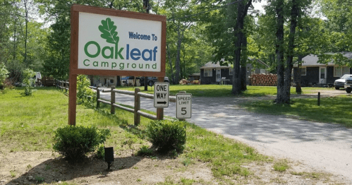 Sign welcoming visitors to Oakleaf Campground, with a one-way and speed limit sign visible in a wooded area.