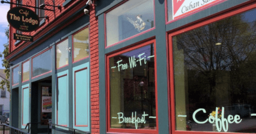 Exterior of a café with a sign reading "The Lodge," featuring windows advertising free Wi-Fi, breakfast, and coffee.