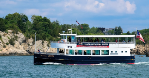 A scenic boat named "Coastal Queen" cruises on calm waters near rocky shores, with passengers enjoying the view.