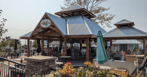 A lively outdoor dining area with a large pavilion, surrounded by greenery and patrons enjoying their meals.