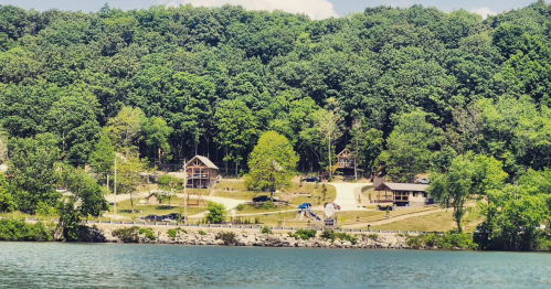 A serene lakeside view with green trees, houses, and a playground along the shore.