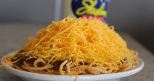 A plate of spaghetti topped with a generous mound of shredded cheddar cheese.