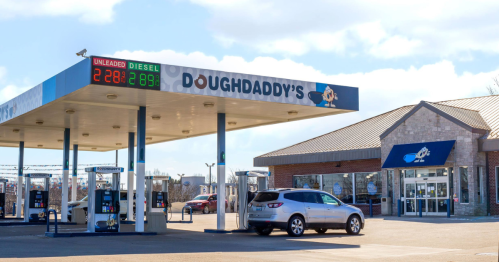 Gas station with a sign displaying fuel prices, featuring "DoughDaddy's" branding and a car parked nearby.