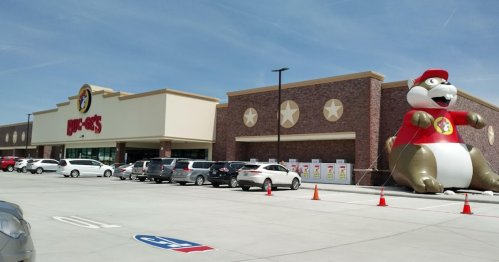 A large Buc-ee's store with a giant inflatable beaver mascot outside, surrounded by parked cars on a sunny day.