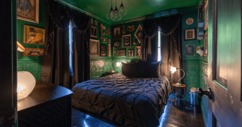 A cozy bedroom with dark green walls, black bedding, and framed art, featuring curtains and stylish lighting.