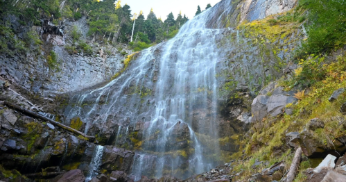 A cascading waterfall flows down a rocky cliff, surrounded by lush greenery and trees.