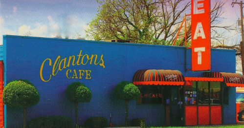Bright blue building with "Clanton's Cafe" sign and red "EAT" marquee, featuring trimmed bushes in front.