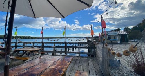 A scenic view of a waterfront dock with colorful buoys, picnic tables, and a cloudy sky.