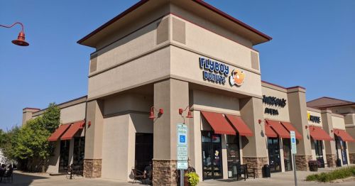 Exterior of Flyboy Donuts shop with orange awnings and signage, located in a commercial area. Clear blue sky above.