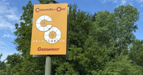 Sign for the Chesapeake and Ohio Greenway, featuring a colorful design and surrounded by green trees.