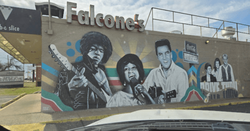 Mural featuring iconic musicians, including a guitarist, singer, and Elvis, on the side of a building.