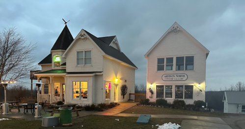 A charming two-story building with a turret, featuring a gallery sign and warm lights against a cloudy sky.