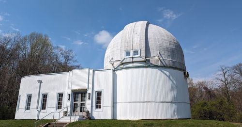 A white observatory building with a large dome, surrounded by trees and a clear blue sky.