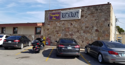 Exterior of the Friendship Inn restaurant, featuring a stone wall and parked cars in front.