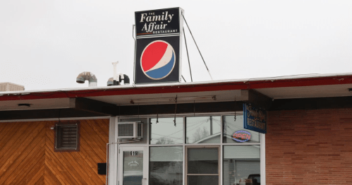 Sign for "The Family Affair Restaurant" with a Pepsi logo, featuring a large window and an "Open" sign.