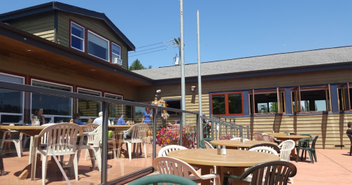 Outdoor dining area of a restaurant with tables and chairs, surrounded by a railing and a sunny blue sky.