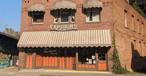 A brick building with a striped awning, featuring the sign "Carlson's" and "The Carbon Block" above the entrance.