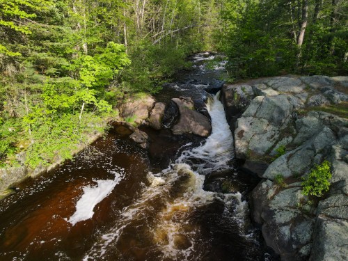 A serene river flows over rocks, surrounded by lush green trees in a peaceful natural setting.