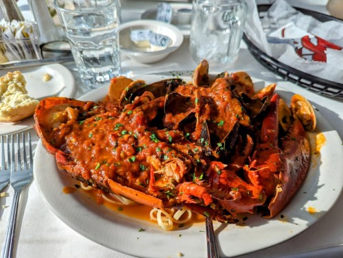 A plate of lobster and mussels in a rich tomato sauce, served over pasta, garnished with parsley.