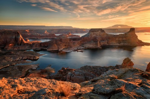 Sunset over a serene lake surrounded by rugged cliffs and rock formations, with a colorful sky reflecting on the water.
