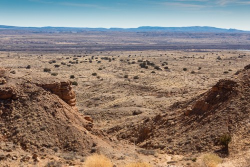 A vast desert landscape with rocky formations and sparse vegetation under a clear blue sky.